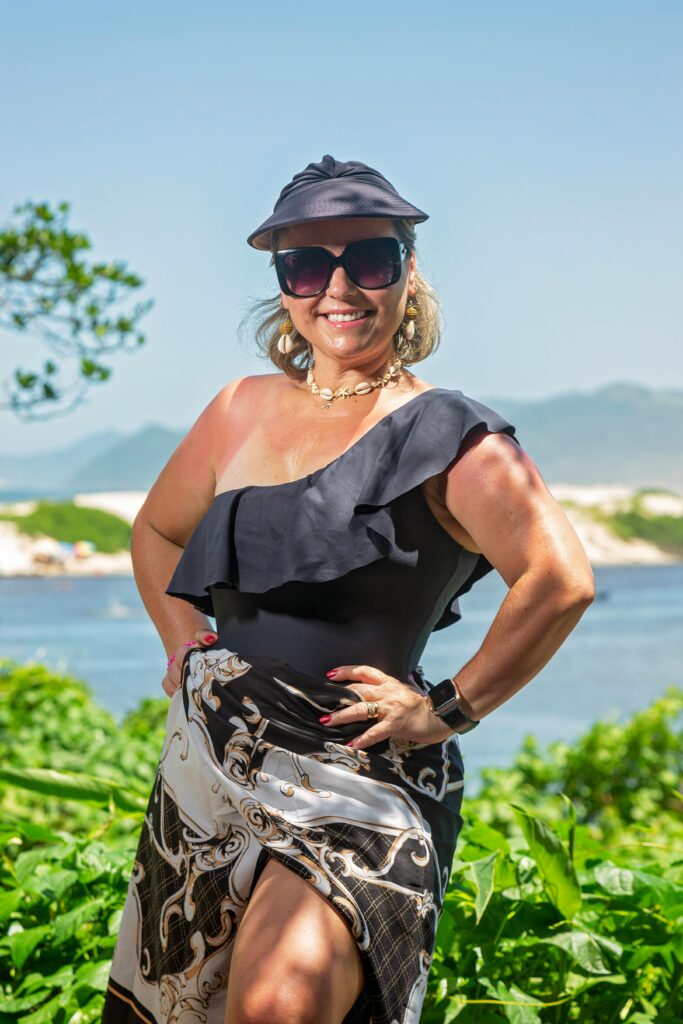 Confident woman in stylish summer outfit poses outdoors with scenic background.