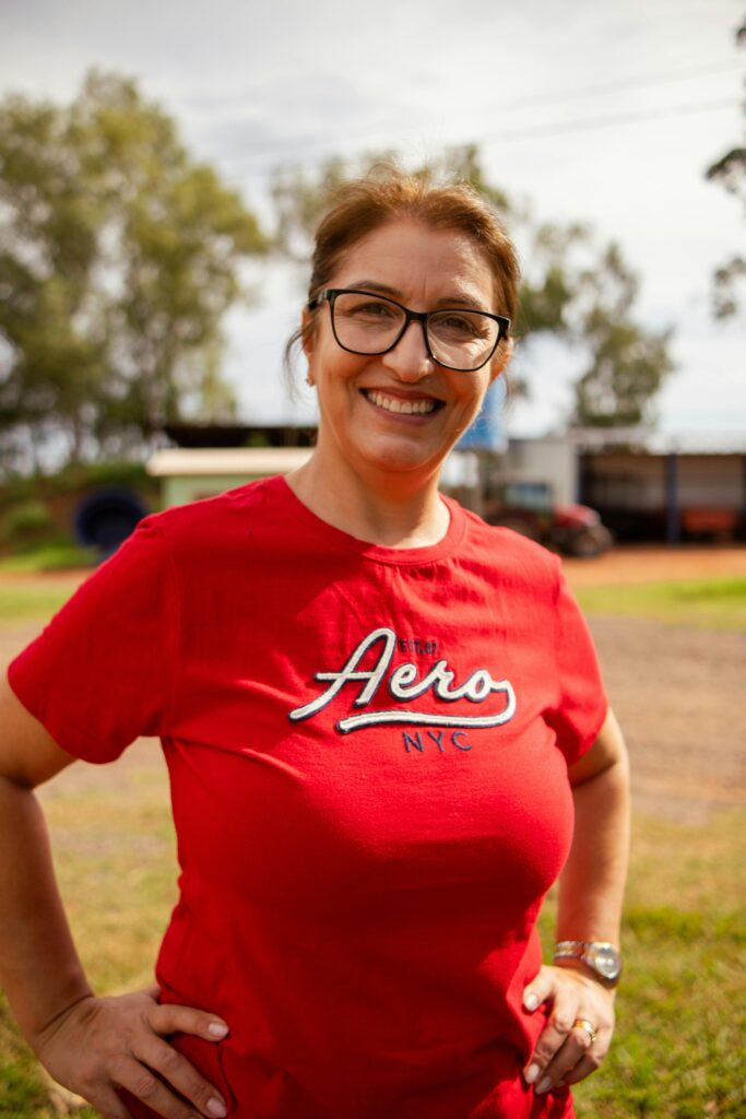 Smiling woman in red t-shirt at a Brazilian orange farm, showcasing rural life in Nova Aliança do Ivaí.